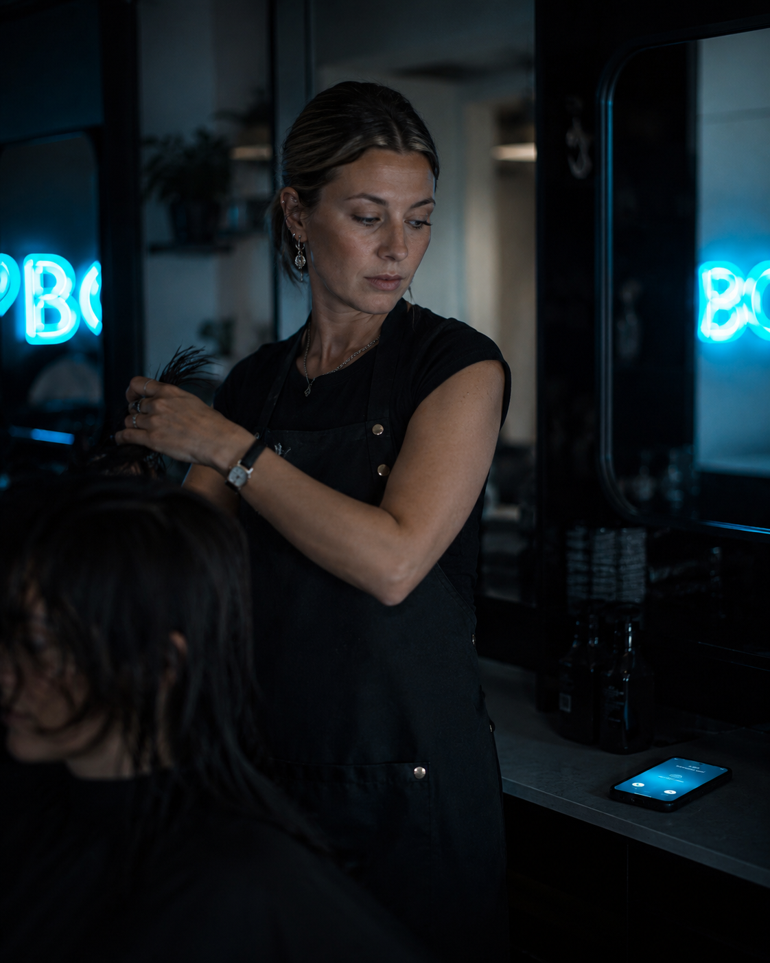 Australian hairstylist with hands in client's hair, phone lights up beside her